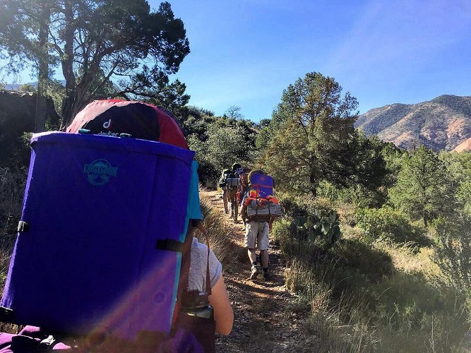 Group backpacking on a trail with crazy creek chairs on the outside of their bags.